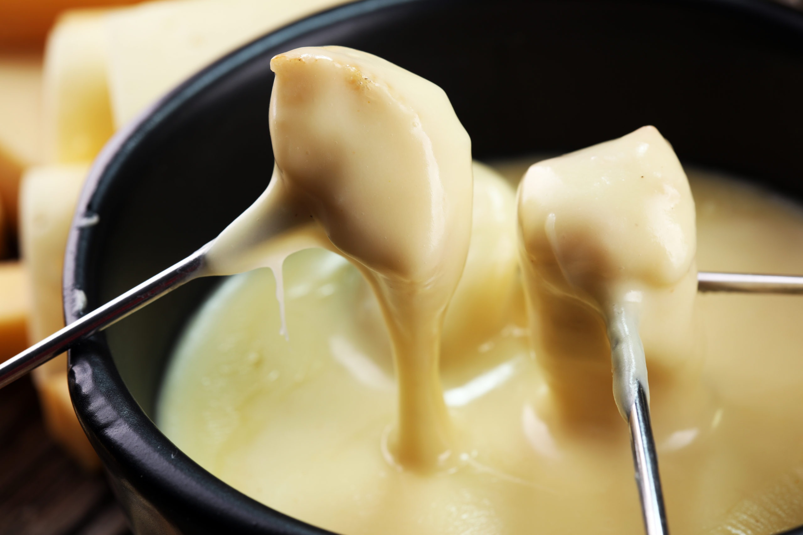 Gourmet Swiss fondue dinner on a winter evening with assorted cheeses on a board alongside a heated pot of cheese fondue with two forks dipping bread and white wine behind in a tavern or restaurant